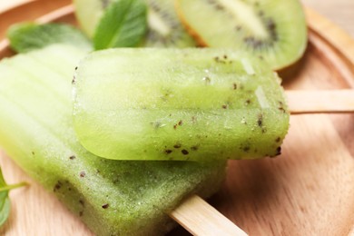 Tasty kiwi ice pops on wooden plate, closeup. Fruit popsicle