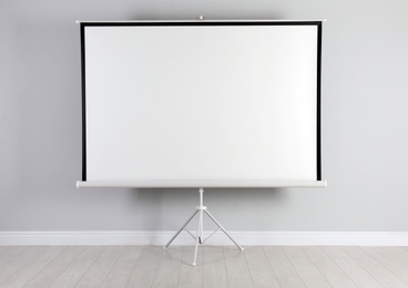 Photo of Blank projection screen near white wall indoors. Space for design
