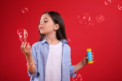 Little girl blowing soap bubbles on red background