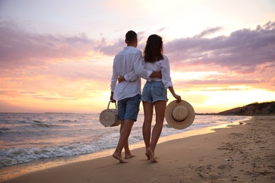 Photo of Lovely couple walking on beach at sunset, back view