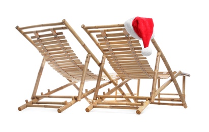 Wooden deck chairs and Santa Claus hat on white background. Christmas vacation