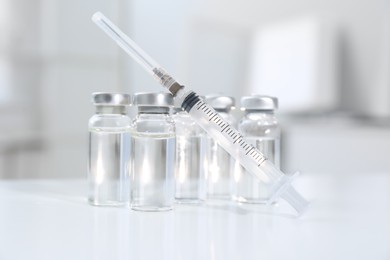 Syringe with vials of medicine on white table, closeup