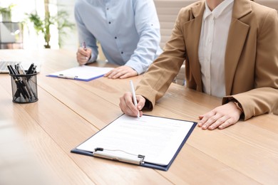 Woman signing contract at table in office, closeup.