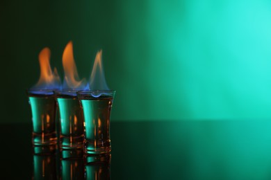 Flaming vodka in shot glasses on green background, space for text