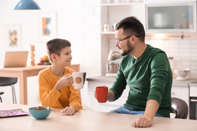 Photo of Little boy and his dad drinking tea together in kitchen