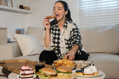 Happy overweight woman eating pizza and chips on sofa at home