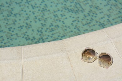 Photo of Stylish sunglasses near outdoor swimming pool on sunny day, space for text. Beach accessory