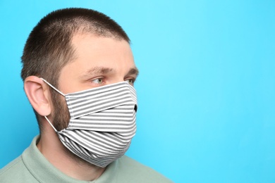 Man wearing handmade cloth mask on light blue background, space for text. Personal protective equipment during COVID-19 pandemic
