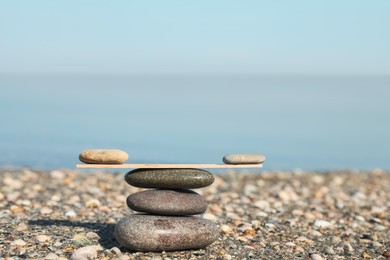 Stack of stones with wooden stick on beach, space for text. Harmony and balance concept