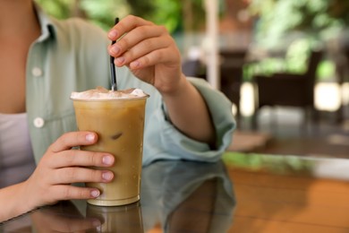 Woman with plastic takeaway cup of delicious iced coffee at table in outdoor cafe, closeup. Space for text