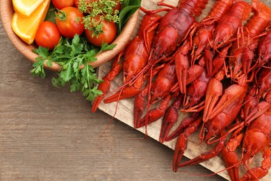 Delicious red boiled crayfish and products in bowl on wooden table, top view