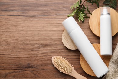 Dry shampoo sprays, green leaves and hairbrush on wooden table, flat lay. Space for text