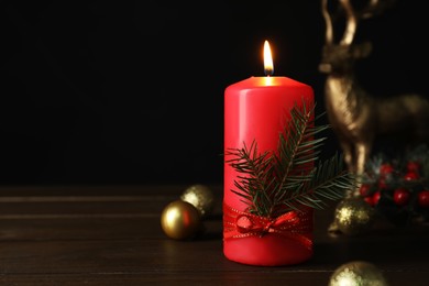 Red burning candle and Christmas decor on wooden table against black background. Space for text