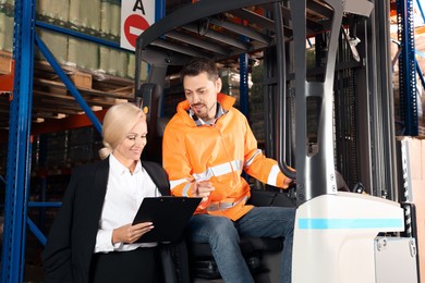Worker talking with manager while sitting in forklift truck at warehouse