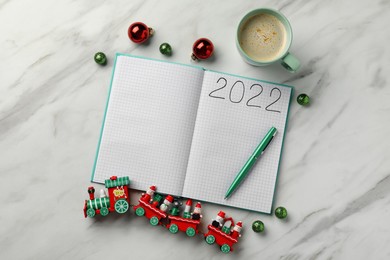 Open planner, cup of coffee and Christmas decor on white marble background, flat lay. 2022 New Year aims