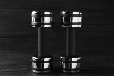 Two metal dumbbells on black wooden table