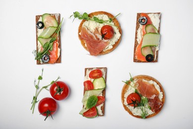 Tasty rusks and rye crispbreads with different toppings on white background, top view