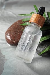 Bottle of face serum, spa stones and leaf on wet grey marble table, closeup