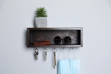 Wooden hanger for keys with wallet, sunglasses, medical masks and houseplant on white wall