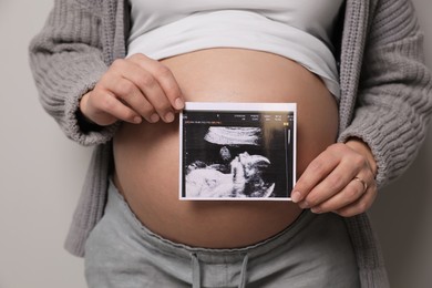 Young pregnant woman with ultrasound picture of baby on grey background, closeup
