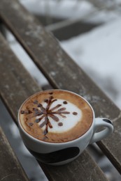 Photo of Cup of aromatic coffee on wooden bench outdoors in winter