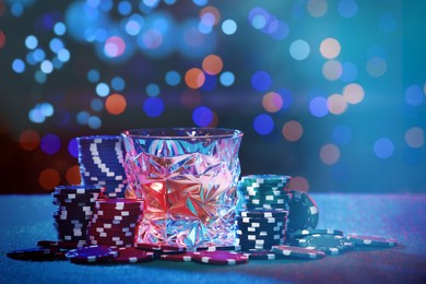 Alcohol drink and casino chips on table against blurred lights. Bokeh effect
