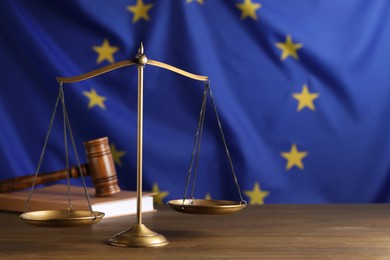 Scales of justice, judge's gavel and book on wooden table against European Union flag