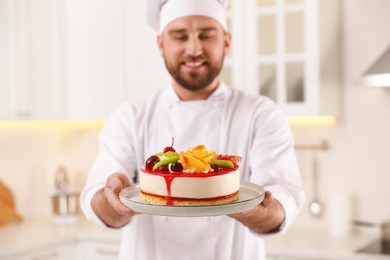 Photo of Happy professional confectioner holding delicious cake in kitchen, focus on hands