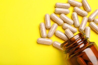 Many gelatin capsules and bottle on yellow background, flat lay. Space for text