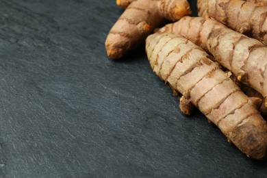 Photo of Many raw turmeric roots on black textured table, closeup. Space for text