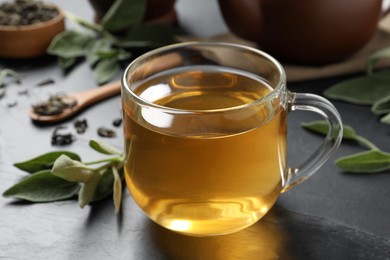 Cup of aromatic sage tea on black table
