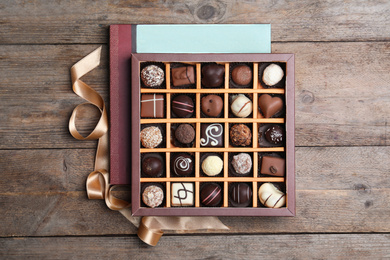Photo of Box with tasty chocolate candies on wooden table, flat lay