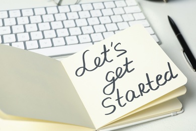 Notebook with phrase Let's Get Started and keyboard on white table