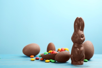Chocolate Easter bunny, candies and eggs on light blue wooden table. Space for text