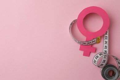 Photo of Female gender sign and measuring tape on pink background, flat lay. Space for text