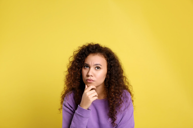 Pensive African-American woman on yellow background. Thinking about difficult question