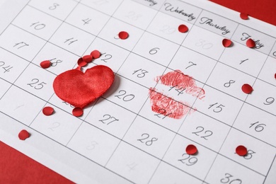 Calendar with marked Valentine's Day, confetti and heart on red background, closeup