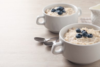 Tasty oatmeal porridge with blueberries served on light wooden table, space for text