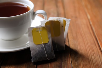 Tea bags near cup of hot drink on wooden table, closeup