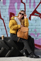 Photo of Young woman with stylish backpack near brick wall outdoors