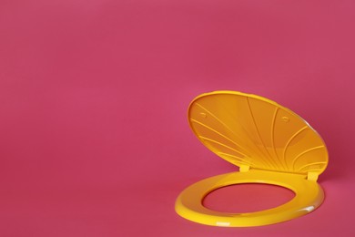 New yellow plastic toilet seat on pink background, space for text