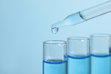 Dripping reagent into test tube on light blue background, closeup. Laboratory analysis