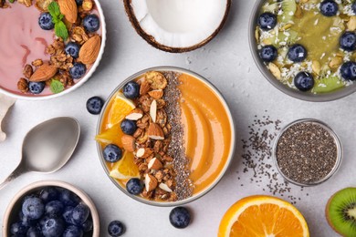 Bowls with different delicious smoothies and fresh ingredients on white table, flat lay