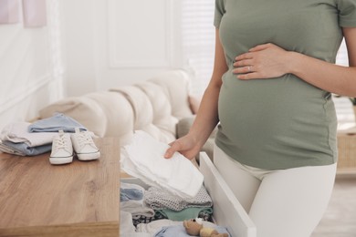 Pregnant woman holding diapers at home, closeup