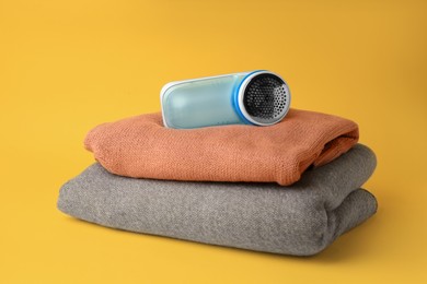 Photo of Modern fabric shaver and woolen clothes on yellow background