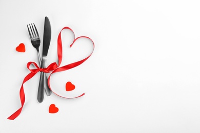 Beautiful cutlery set, hearts and red ribbon on white background, flat lay with space for text. Valentine's Day dinner