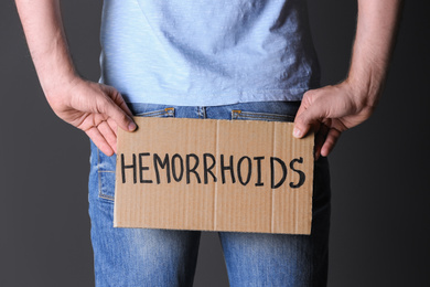 Photo of Man holding carton sign with word HEMORRHOIDS on black background, closeup