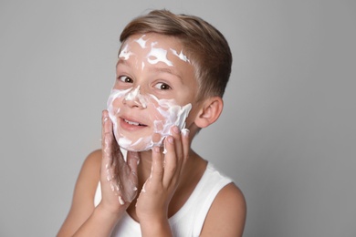 Cute little boy with soap foam on face against gray background