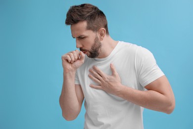 Man coughing on light blue background. Cold symptoms