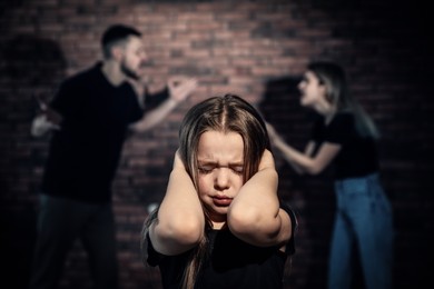 Scared little girl and blurred view of quarrelling parents on background. Domestic violence